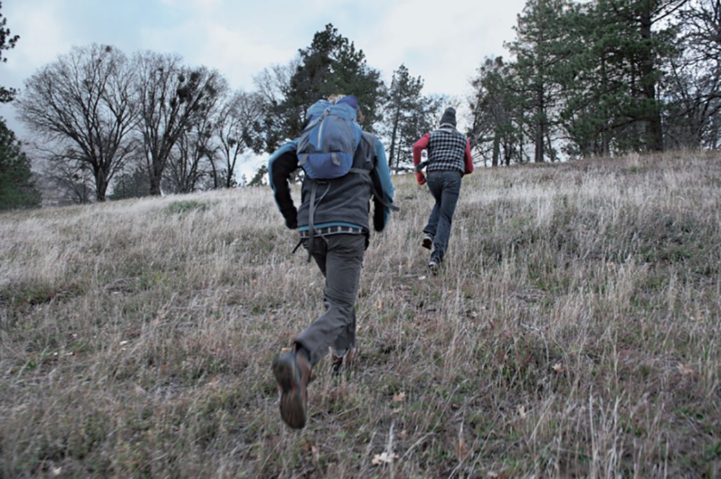 Two people in hiking gear running up a hill