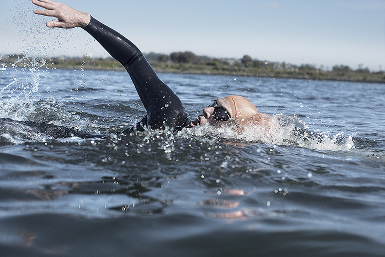 A person swimming in a lake in a swimming cap and full-body wetsuit