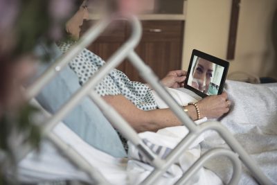 A woman in a hospital bed having a video call with someone on a tablet