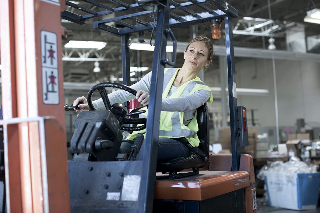 A woman in a reflective vest operating a forklift in a warehouse