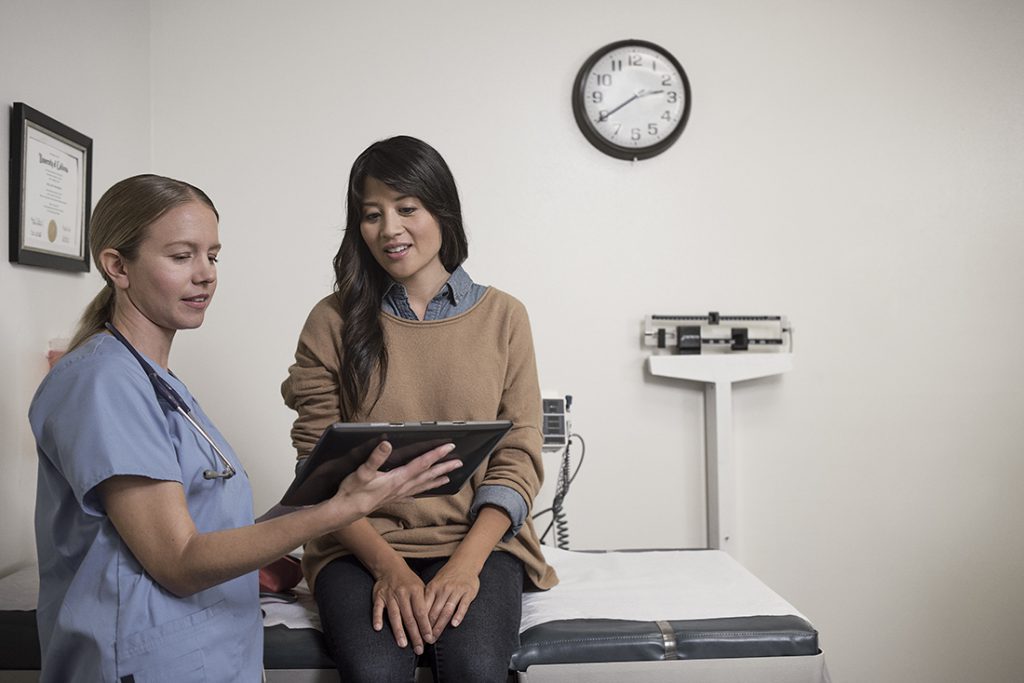 Female nurse and patient looking at a tablet in an examination room