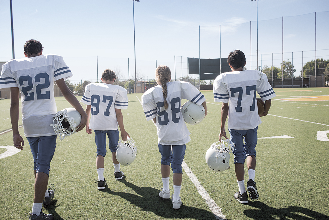 Four children in football uniforms walking onto a field
