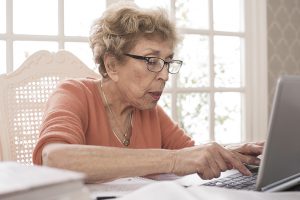 Elderly woman at a table surrounded by papers on a laptop