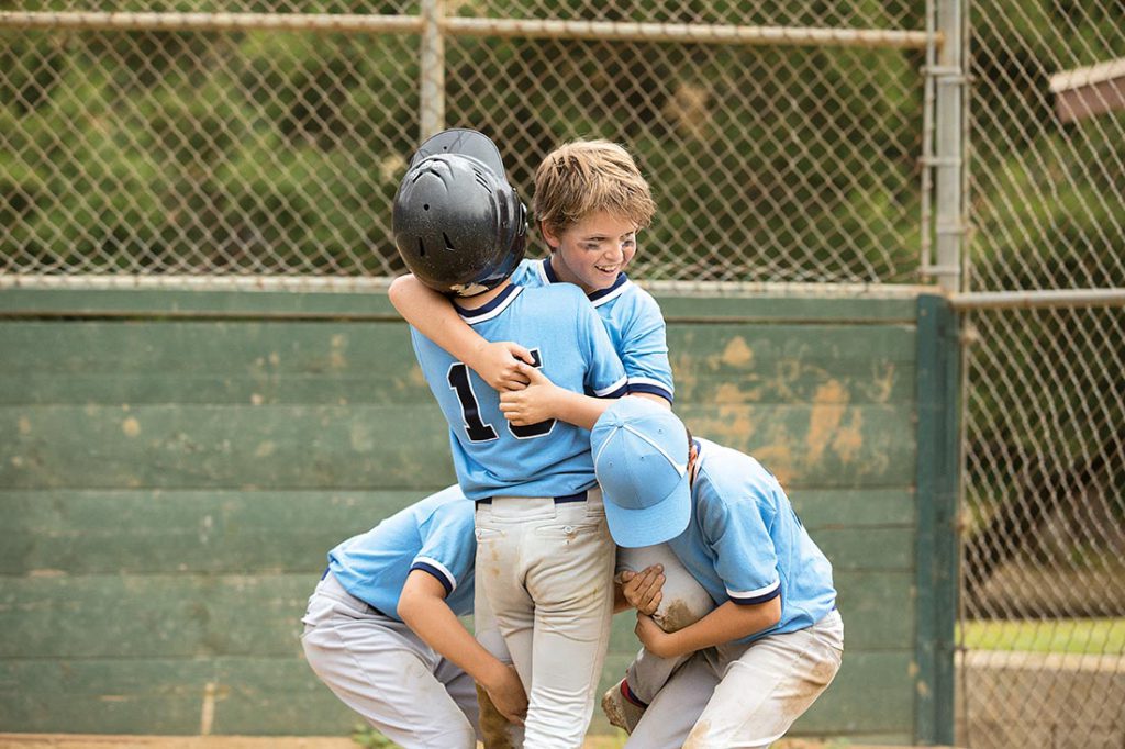 Boys wearing blue baseball uniforms hugging and celebrating