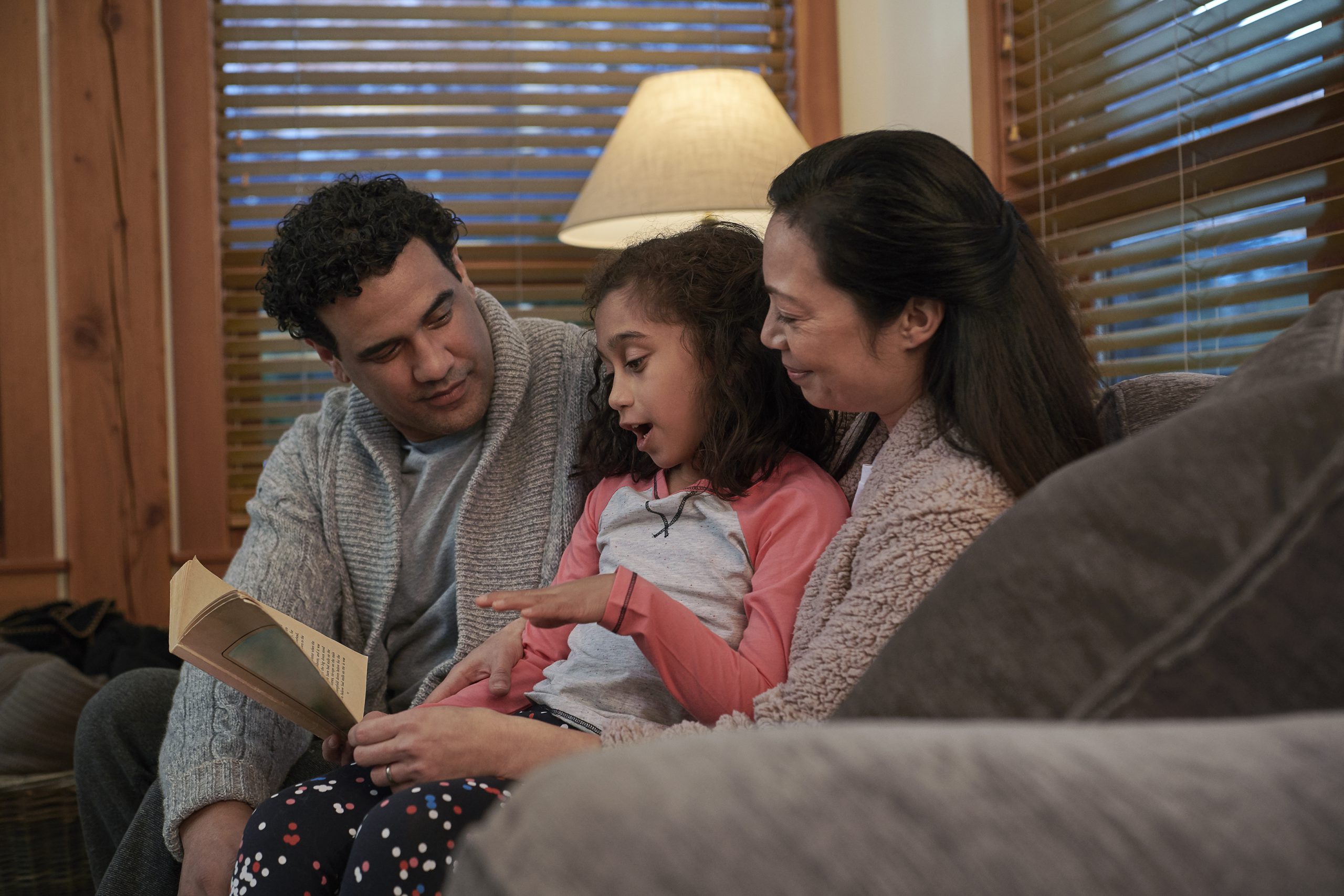 A family of three reading a book on a couch