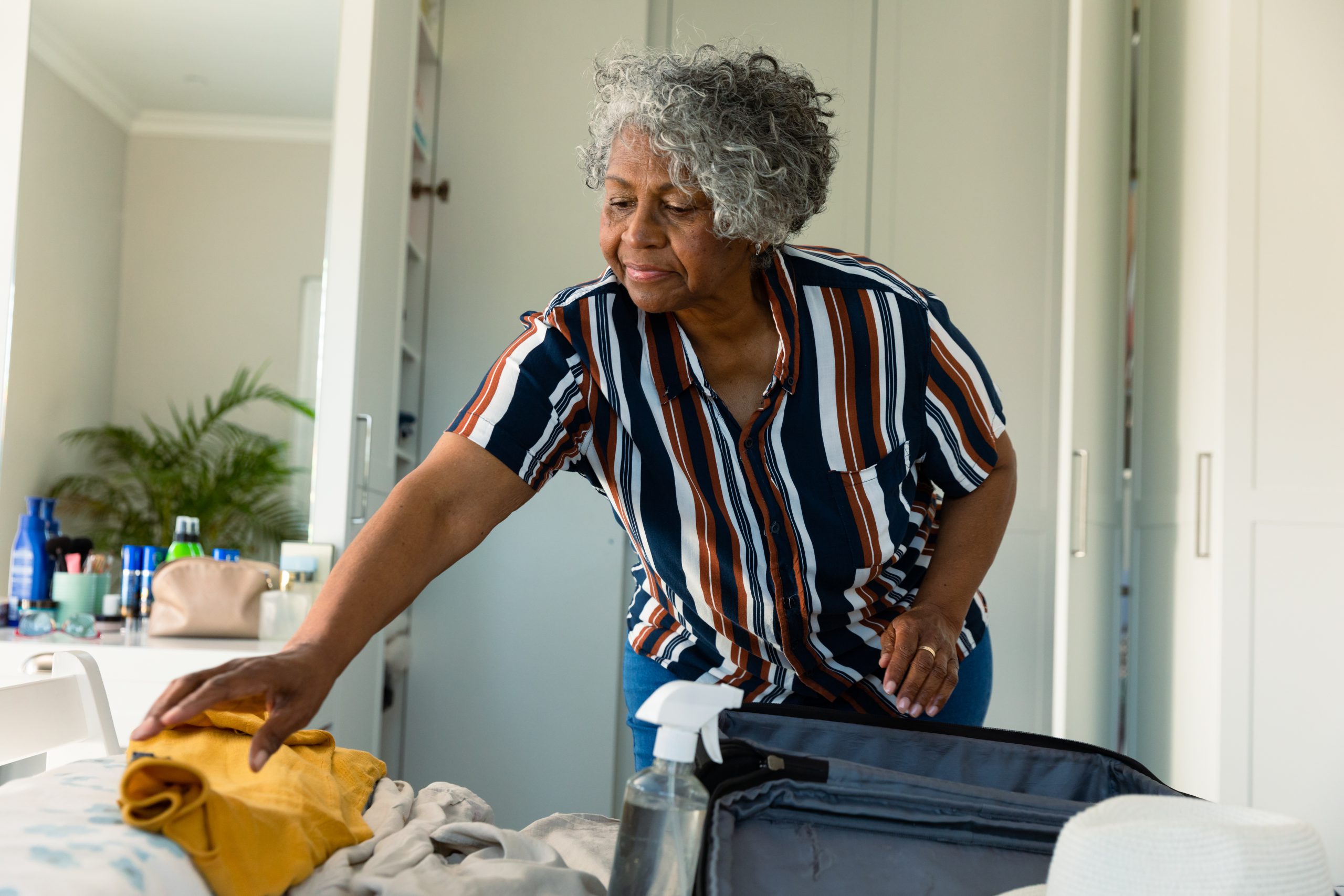 Focused african american senior woman packing suitcase in bedroom.