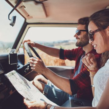 Side view of young couple using a map on a roadtrip for directions. Young man and woman reading a map while sitting in a car.