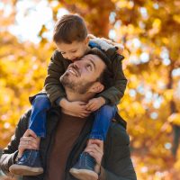 Happy father and little son playing and having fun outdoors over autumn park background