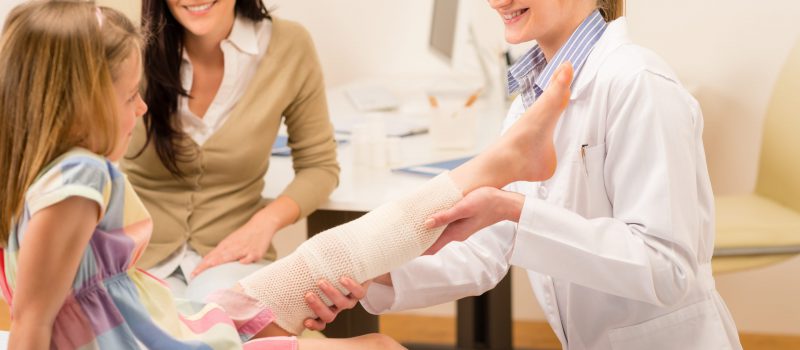 Female pediatrician checking broken bandaged leg of little girl