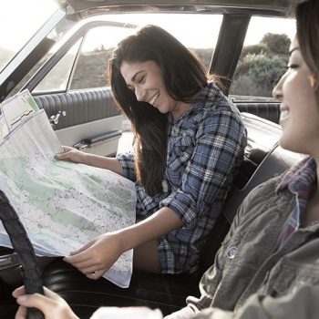 Two women in a vintage car smiling and consulting a large paper map